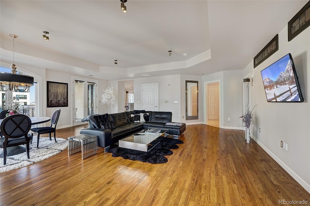 living area with a tray ceiling, an inviting chandelier, wood finished floors, and baseboards