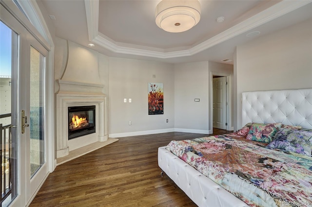 bedroom featuring a large fireplace, dark wood-style flooring, baseboards, ornamental molding, and a tray ceiling