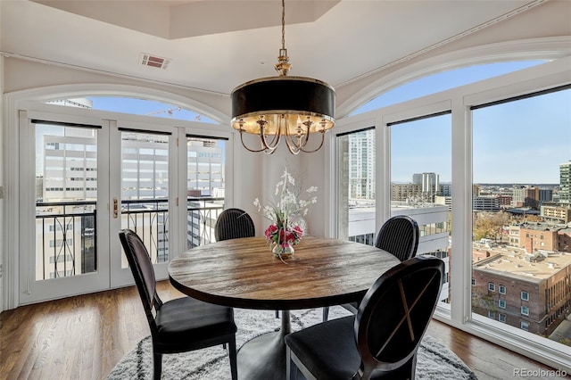 dining space featuring a view of city, a healthy amount of sunlight, visible vents, and wood finished floors