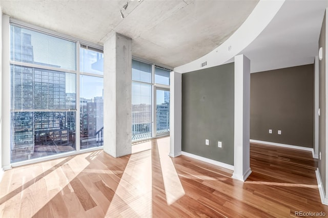 unfurnished room featuring visible vents, baseboards, wood finished floors, a wall of windows, and a city view