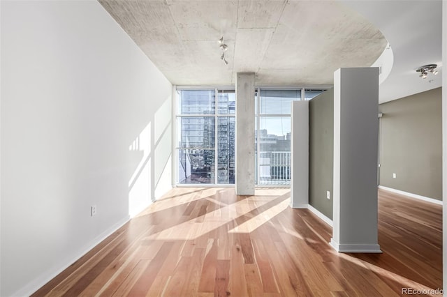 unfurnished room with a wall of windows, baseboards, and wood finished floors