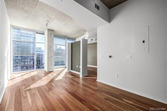 empty room featuring wood finished floors, visible vents, baseboards, electric panel, and floor to ceiling windows