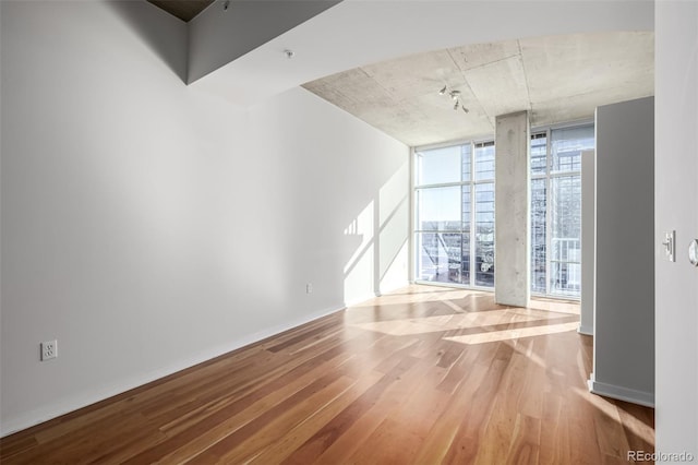 spare room with rail lighting, expansive windows, baseboards, and wood finished floors