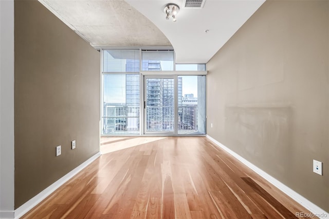 unfurnished room featuring a city view, visible vents, expansive windows, wood finished floors, and baseboards