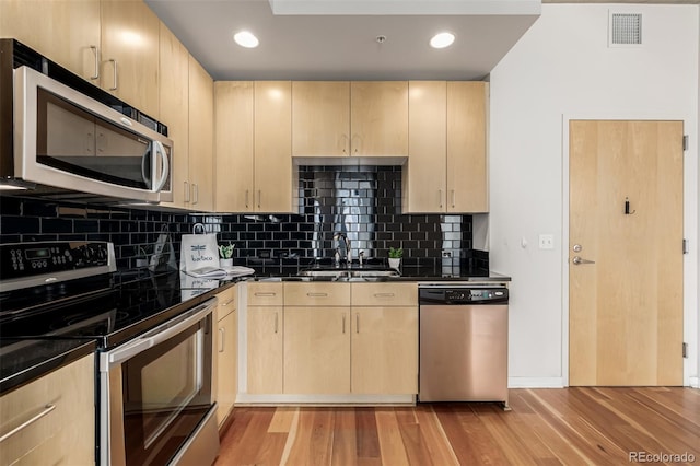 kitchen with light wood finished floors, dark countertops, light brown cabinetry, appliances with stainless steel finishes, and a sink