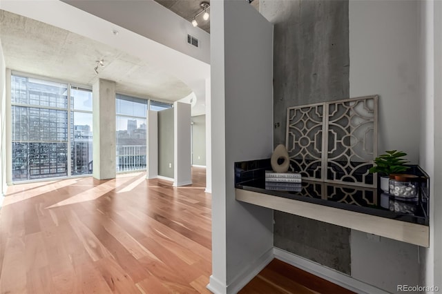 interior space with rail lighting, visible vents, a wall of windows, and wood finished floors