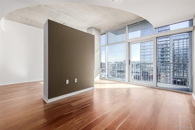 empty room with baseboards, arched walkways, wood finished floors, and floor to ceiling windows