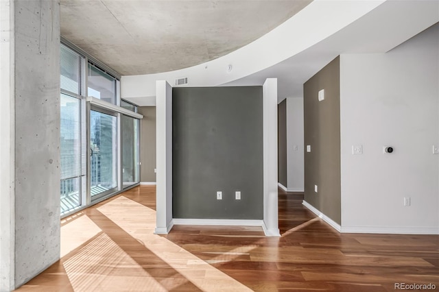 empty room featuring baseboards, expansive windows, visible vents, and wood finished floors