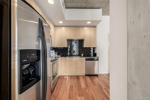 kitchen featuring light brown cabinets, a sink, light wood-style floors, appliances with stainless steel finishes, and dark countertops