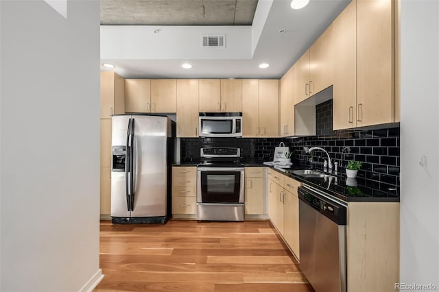 kitchen with visible vents, dark countertops, appliances with stainless steel finishes, light brown cabinets, and a sink