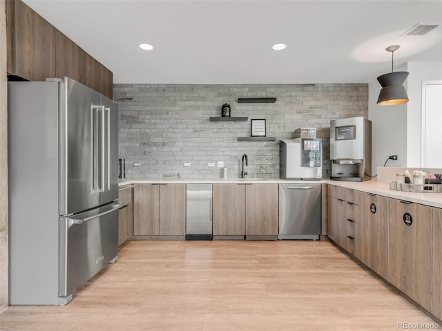 kitchen featuring appliances with stainless steel finishes, light wood-type flooring, a sink, and tasteful backsplash