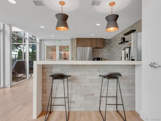 kitchen with freestanding refrigerator, visible vents, light wood-style flooring, and a kitchen breakfast bar