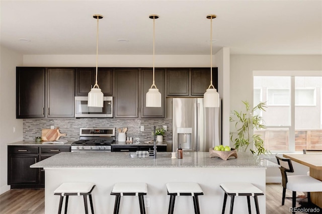 kitchen featuring appliances with stainless steel finishes, a kitchen island with sink, light wood-type flooring, a kitchen bar, and backsplash