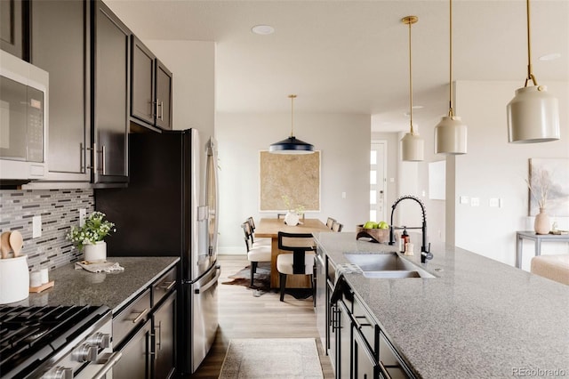 kitchen featuring stainless steel appliances, a sink, wood finished floors, decorative backsplash, and pendant lighting