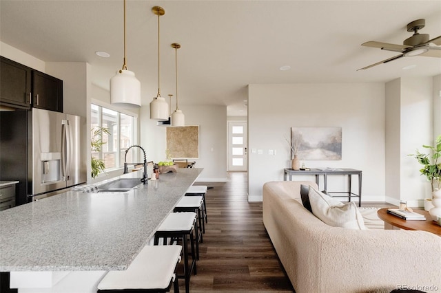 kitchen featuring a breakfast bar area, open floor plan, an island with sink, and stainless steel fridge with ice dispenser