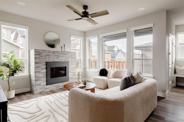 living room with ceiling fan, a stone fireplace, baseboards, and wood finished floors