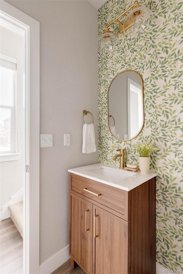 bathroom featuring wood finished floors, vanity, baseboards, and wallpapered walls