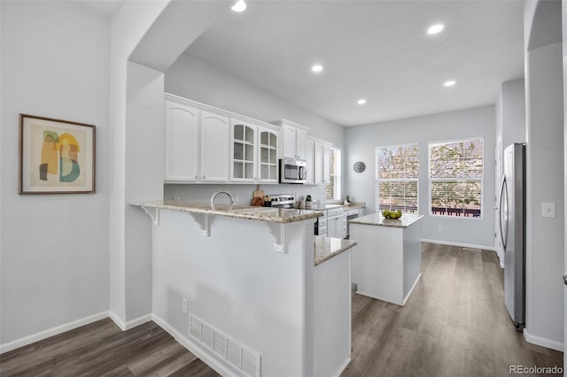 kitchen with a peninsula, white cabinetry, a kitchen island, visible vents, and appliances with stainless steel finishes