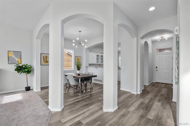 corridor with a chandelier, arched walkways, visible vents, and wood finished floors