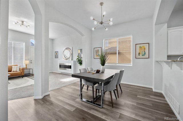 dining area with arched walkways, a notable chandelier, baseboards, and wood finished floors