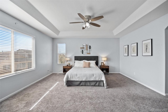 carpeted bedroom featuring a tray ceiling, baseboards, and a ceiling fan