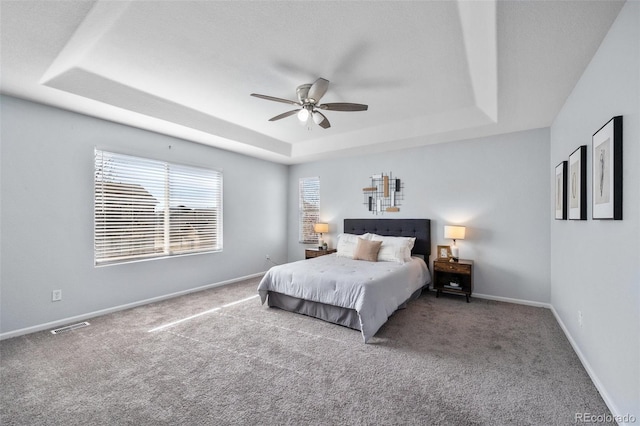 carpeted bedroom featuring visible vents, baseboards, a raised ceiling, and a ceiling fan