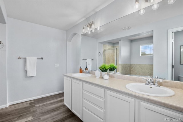full bathroom with a shower stall, wood finished floors, double vanity, and a sink