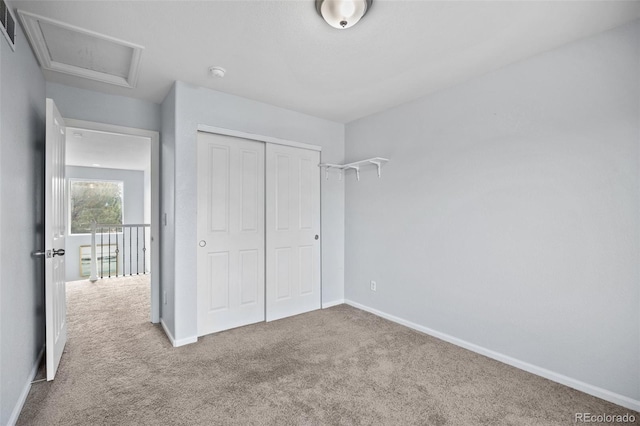 unfurnished bedroom featuring a closet, baseboards, carpet flooring, attic access, and visible vents