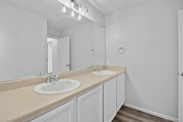 full bath with double vanity, baseboards, a sink, and wood finished floors