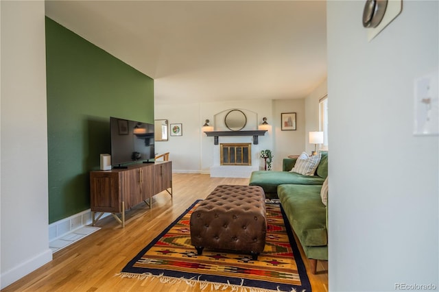 living area featuring a glass covered fireplace, baseboards, and wood finished floors