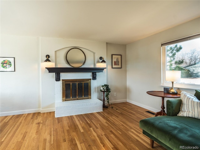 unfurnished living room featuring visible vents, baseboards, a brick fireplace, and wood finished floors