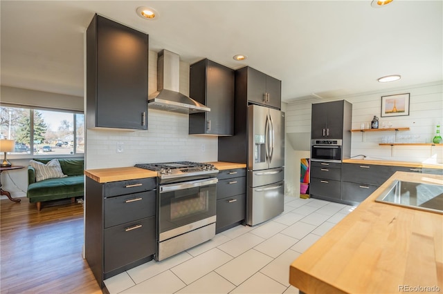 kitchen with backsplash, wall chimney exhaust hood, stainless steel appliances, wood counters, and open shelves