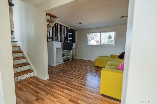 living area featuring visible vents, stairs, baseboards, and wood finished floors