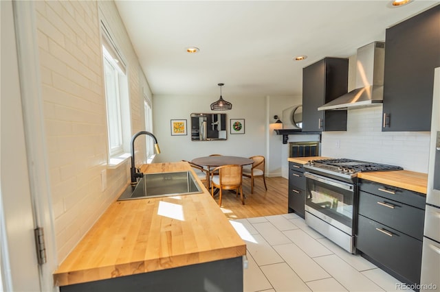 kitchen featuring wall chimney range hood, butcher block countertops, gas range, decorative backsplash, and a sink