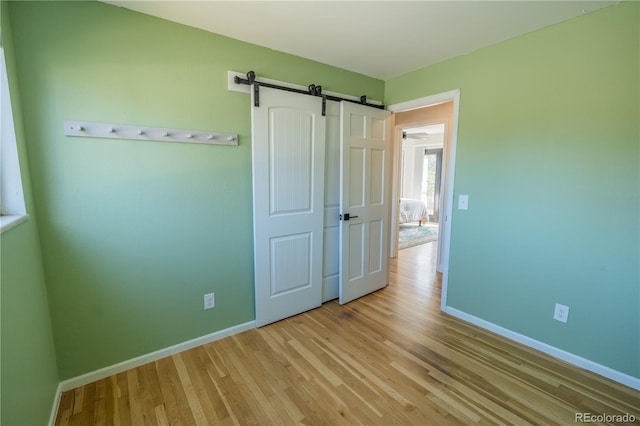 unfurnished bedroom featuring a barn door, light wood-style flooring, and baseboards