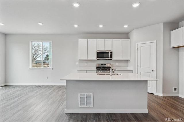 14424 Heritage Dr, Mead, CO 80504 - kitchen with light countertops, wood finished floors, appliances with stainless steel finishes, white cabinets, and an island with sink