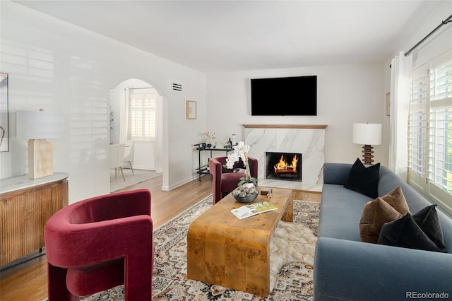 living area featuring arched walkways, wood finished floors, a premium fireplace, and healthy amount of natural light