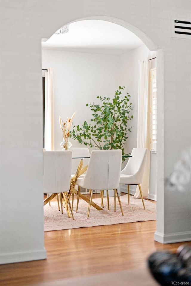 dining space with arched walkways, wood finished floors, and baseboards