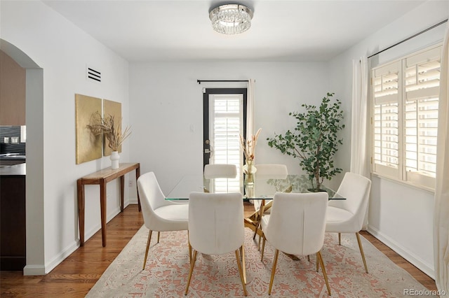 dining space featuring arched walkways, wood finished floors, baseboards, and a chandelier