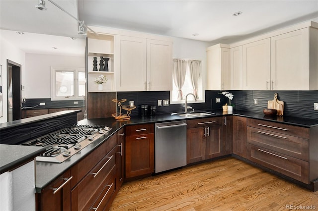 kitchen featuring stainless steel appliances, a sink, white cabinets, light wood-style flooring, and dark countertops