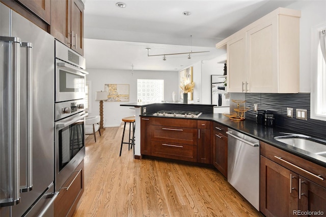kitchen with appliances with stainless steel finishes, a peninsula, light wood-type flooring, dark countertops, and white cabinets