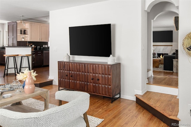 living area featuring a fireplace, light wood-type flooring, baseboards, and arched walkways