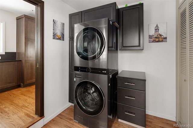 clothes washing area with stacked washer and clothes dryer, cabinet space, light wood finished floors, and baseboards