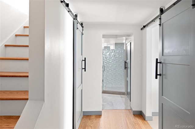 corridor featuring a barn door, stairs, light wood finished floors, and baseboards