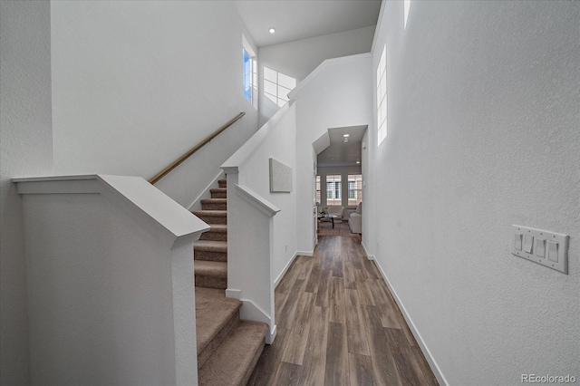 stairs featuring a high ceiling, baseboards, and wood finished floors