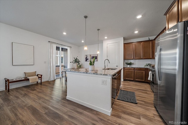 kitchen featuring light stone counters, dark wood-type flooring, a sink, freestanding refrigerator, and a center island with sink