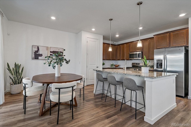 kitchen with stainless steel appliances, light stone counters, an island with sink, and dark wood finished floors