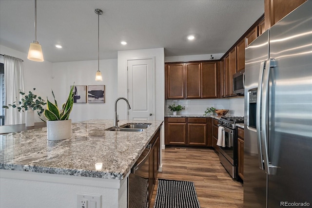 kitchen with dark wood-style flooring, light stone countertops, a kitchen island with sink, stainless steel appliances, and a sink