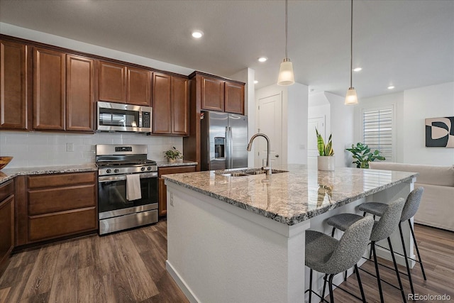 kitchen with tasteful backsplash, dark wood-type flooring, light stone countertops, stainless steel appliances, and a sink