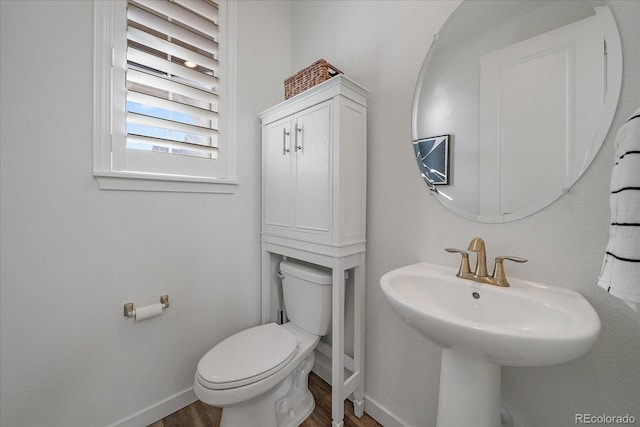 half bathroom with baseboards, a sink, toilet, and wood finished floors